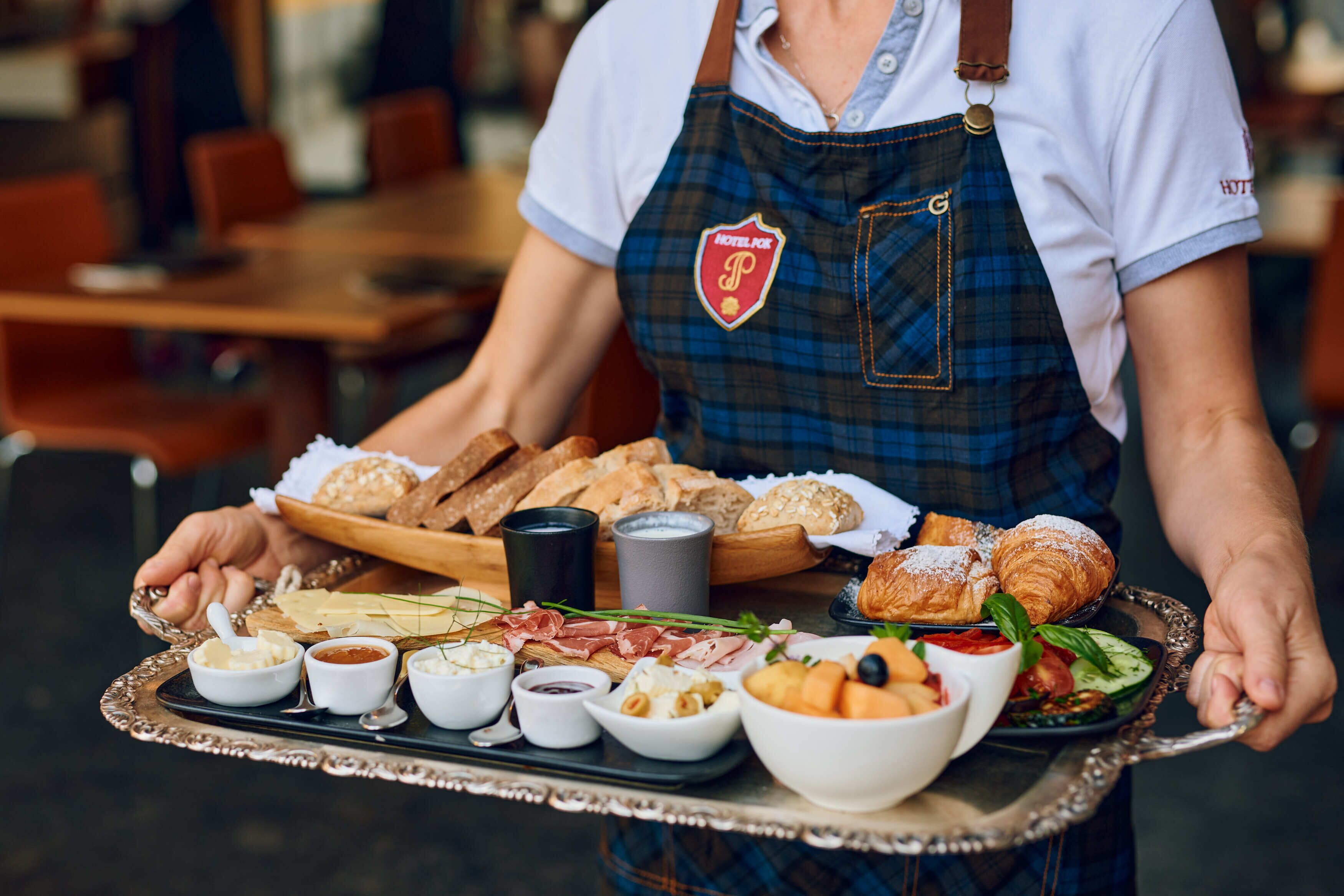 A tray with various food items including bread, pastries, and dips, held by a person wearing a uniform with a logo.