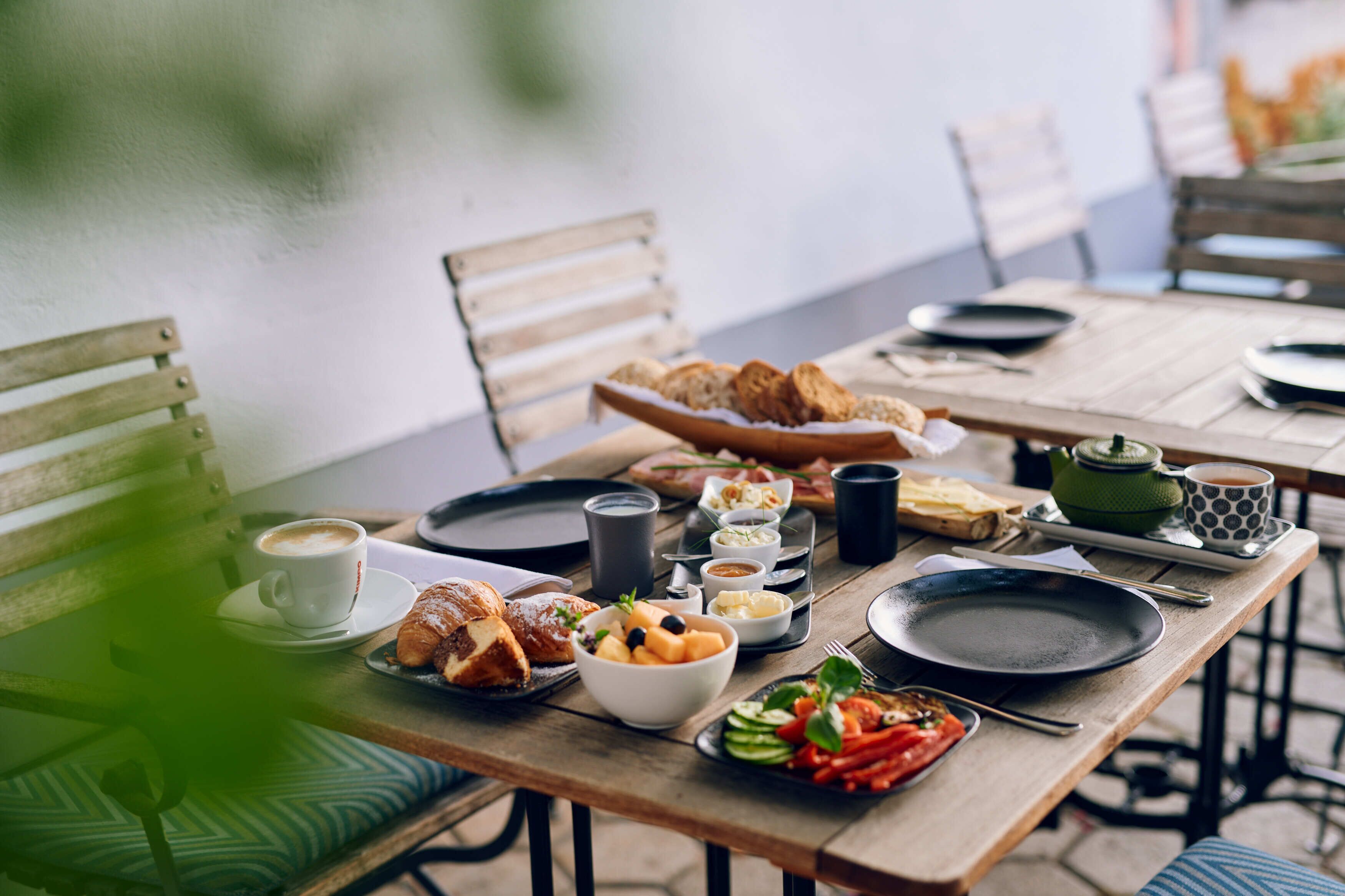Puinen pöytä, joka on katettu aamiaistarvikkeilla: croissantteja, hedelmäkulho ja kuppi kahvia.
