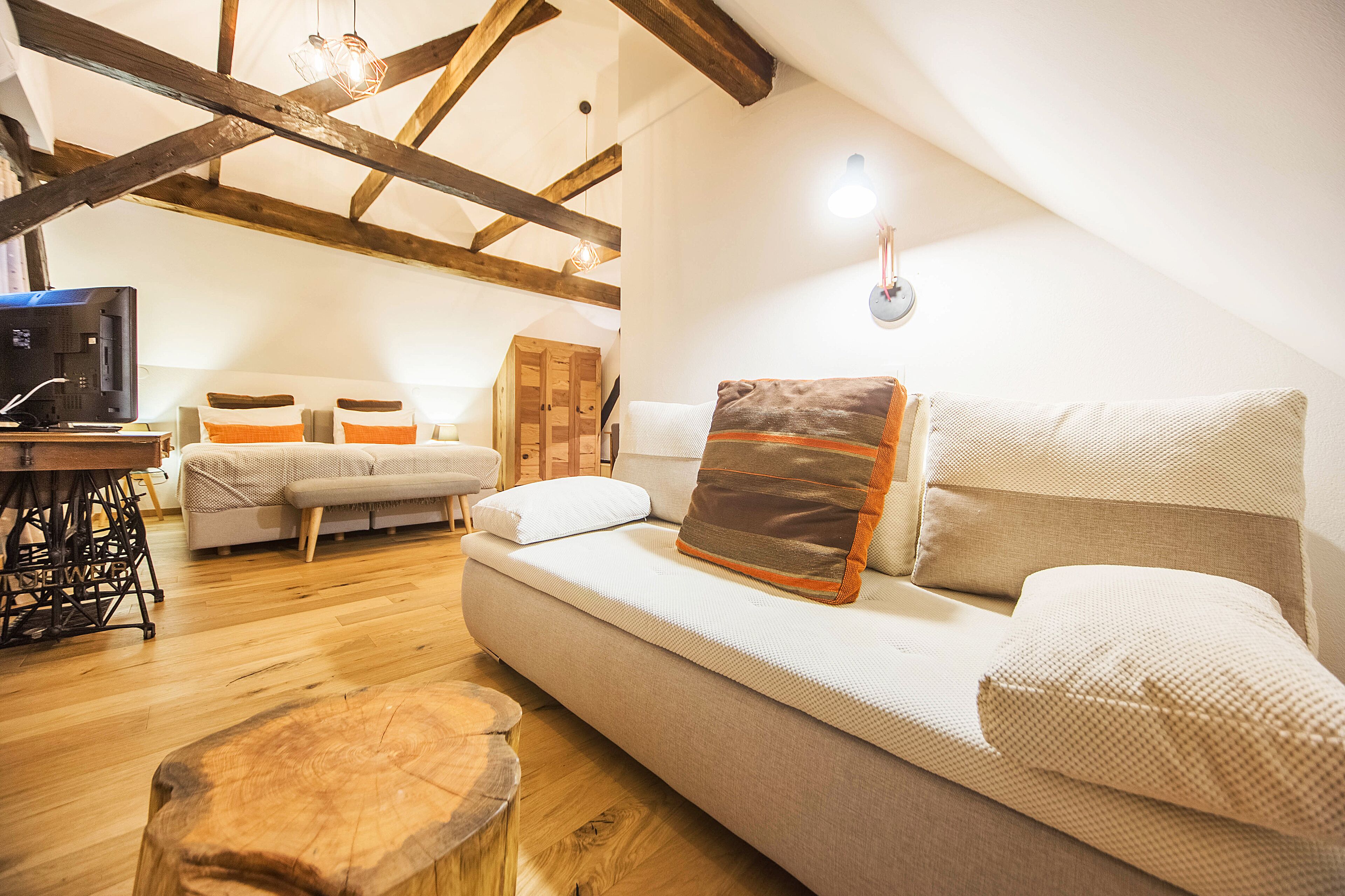 Una sala de estar acogedora con un sofá, vigas de madera, una máquina de coser y un taburete de madera.