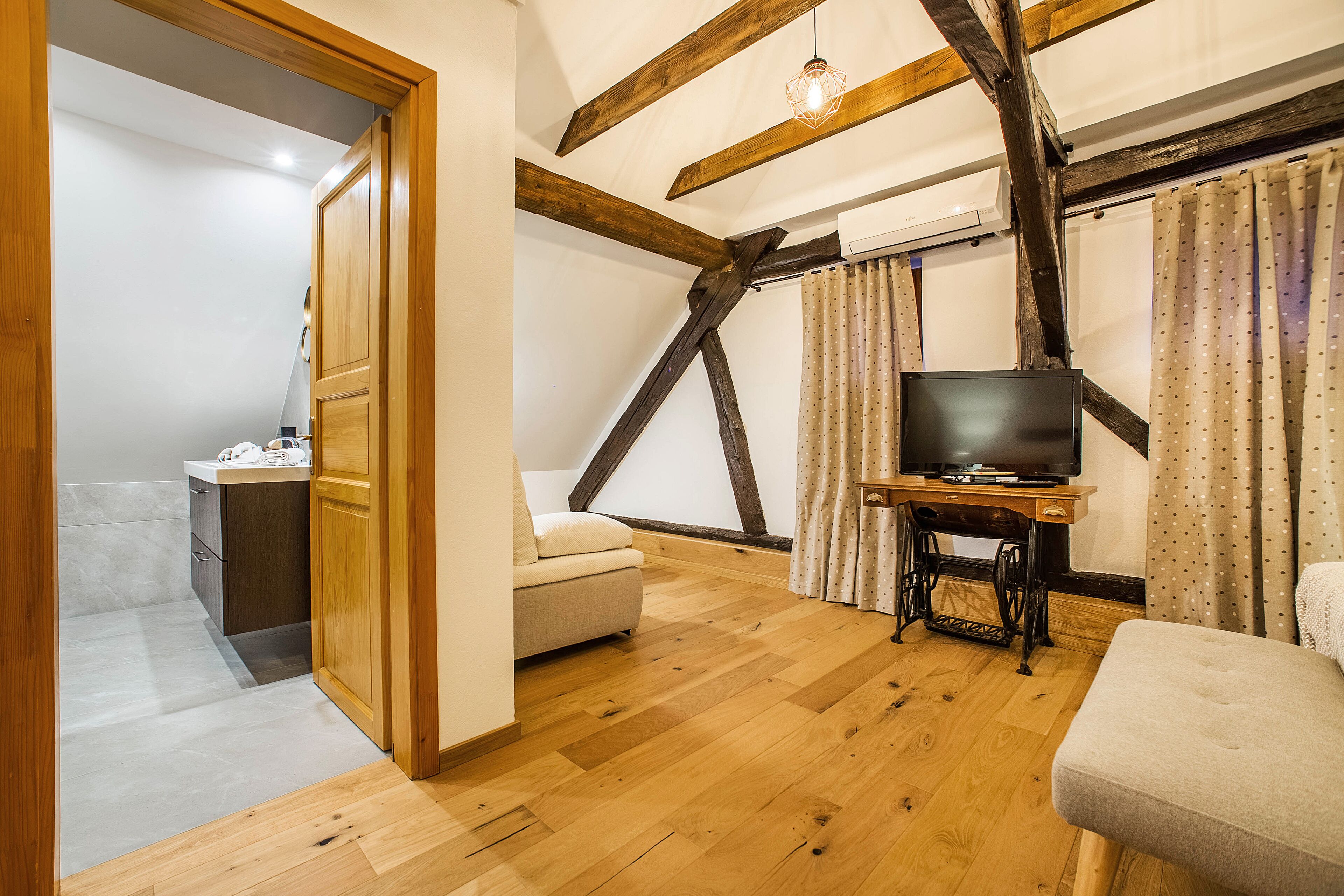 Une pièce avec des poutres en bois, un téléviseur posé sur un meuble en bois, un canapé et une petite table avec une lampe.