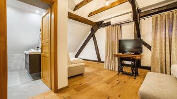 Une pièce avec des poutres en bois, un téléviseur posé sur un meuble en bois, un canapé et une petite table avec une lampe.
