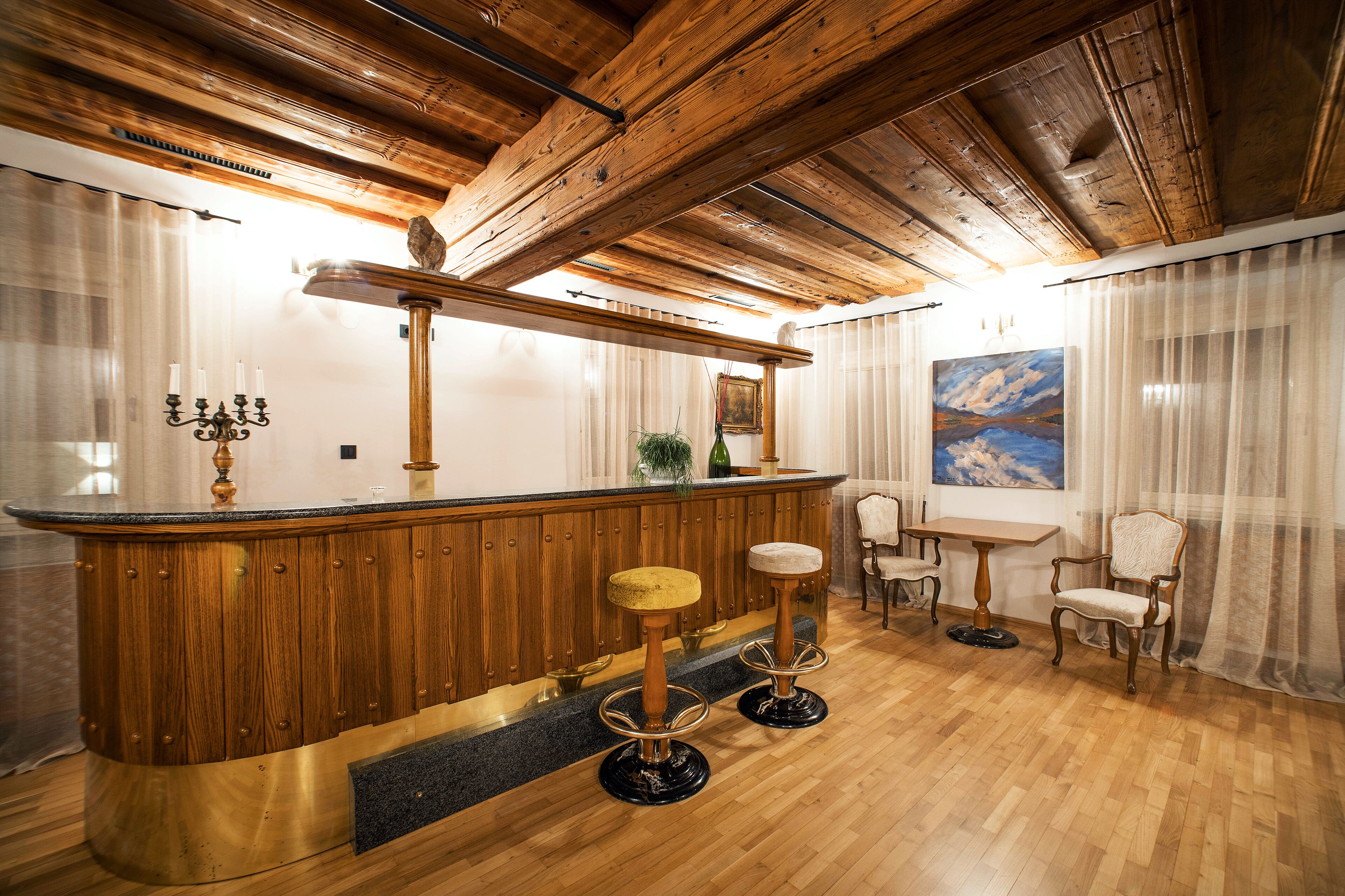 Un área de bar con barra de madera, taburetes, una mesa y sillas.