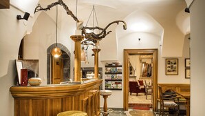 Una hall con una reception in legno, pavimento in pietra, un lampadario e una libreria.
