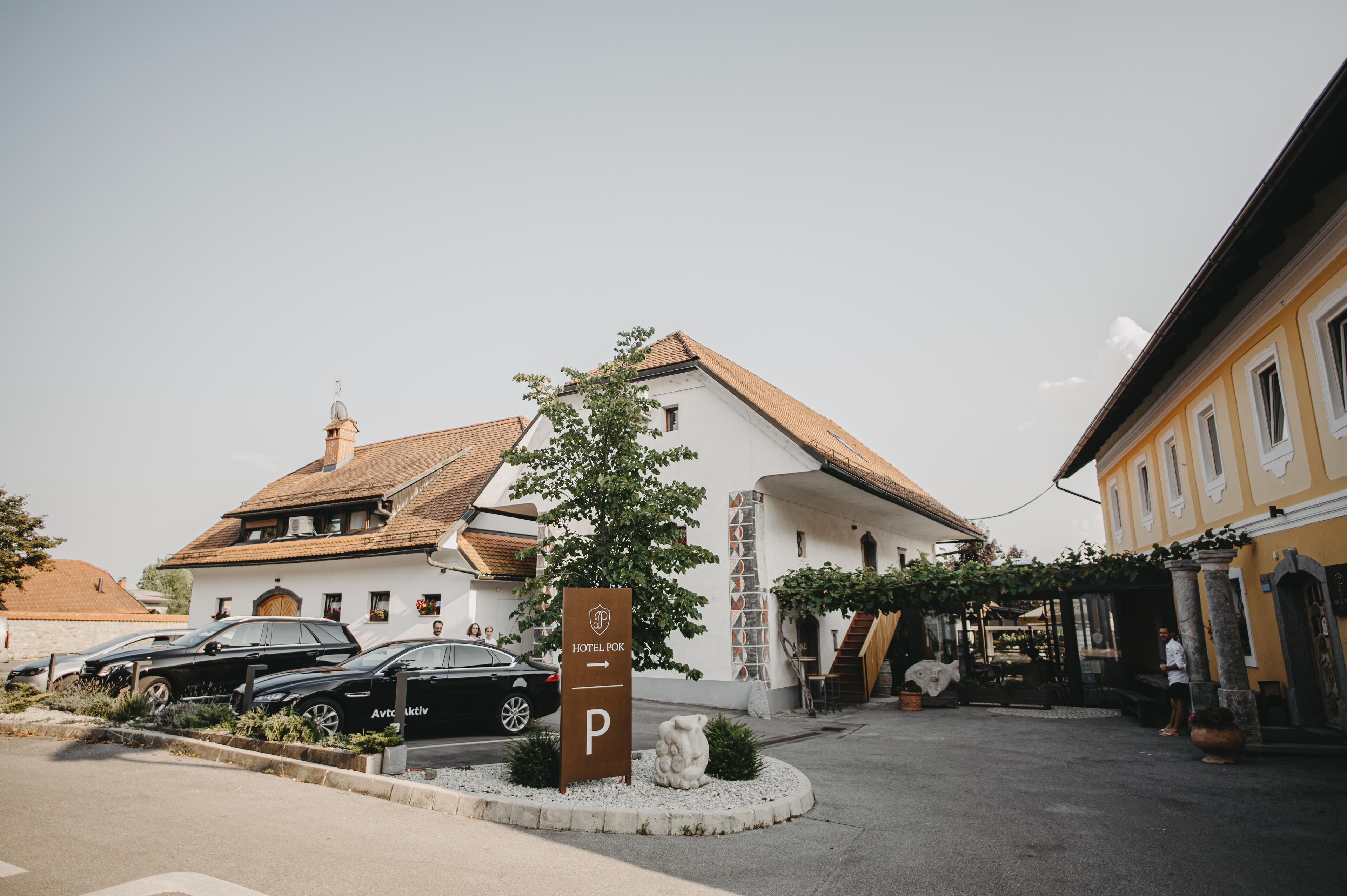 Un hôtel à la façade blanche, doté d’un toit en tuiles et d’un espace de stationnement agrémenté d’un panneau indiquant les places réservées aux clients de l’hôtel.