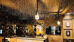 L’intérieur d’un restaurant avec un sol en marbre, des meubles en bois, des luminaires suspendus et un mur en briques.