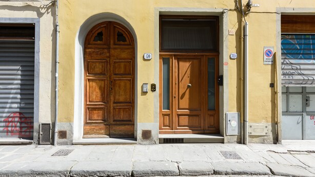 Un bâtiment doté de deux portes en bois, l’une avec un arc en plein cintre et l’autre avec un sommet rectangulaire. Au-dessus des portes, on peut voir deux panneaux : l’un indique le numéro 38 et l’autre affiche le symbole d’interdiction de stationnement.