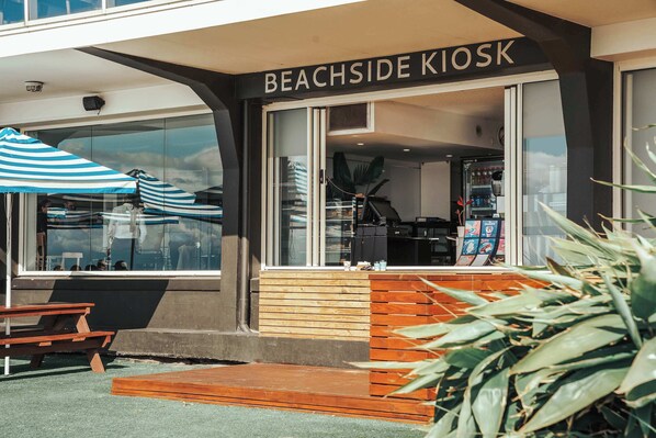 A kiosk named 'Beachside Kiosk' with a wooden bench outside, a striped umbrella, and a view of the interior through the glass.