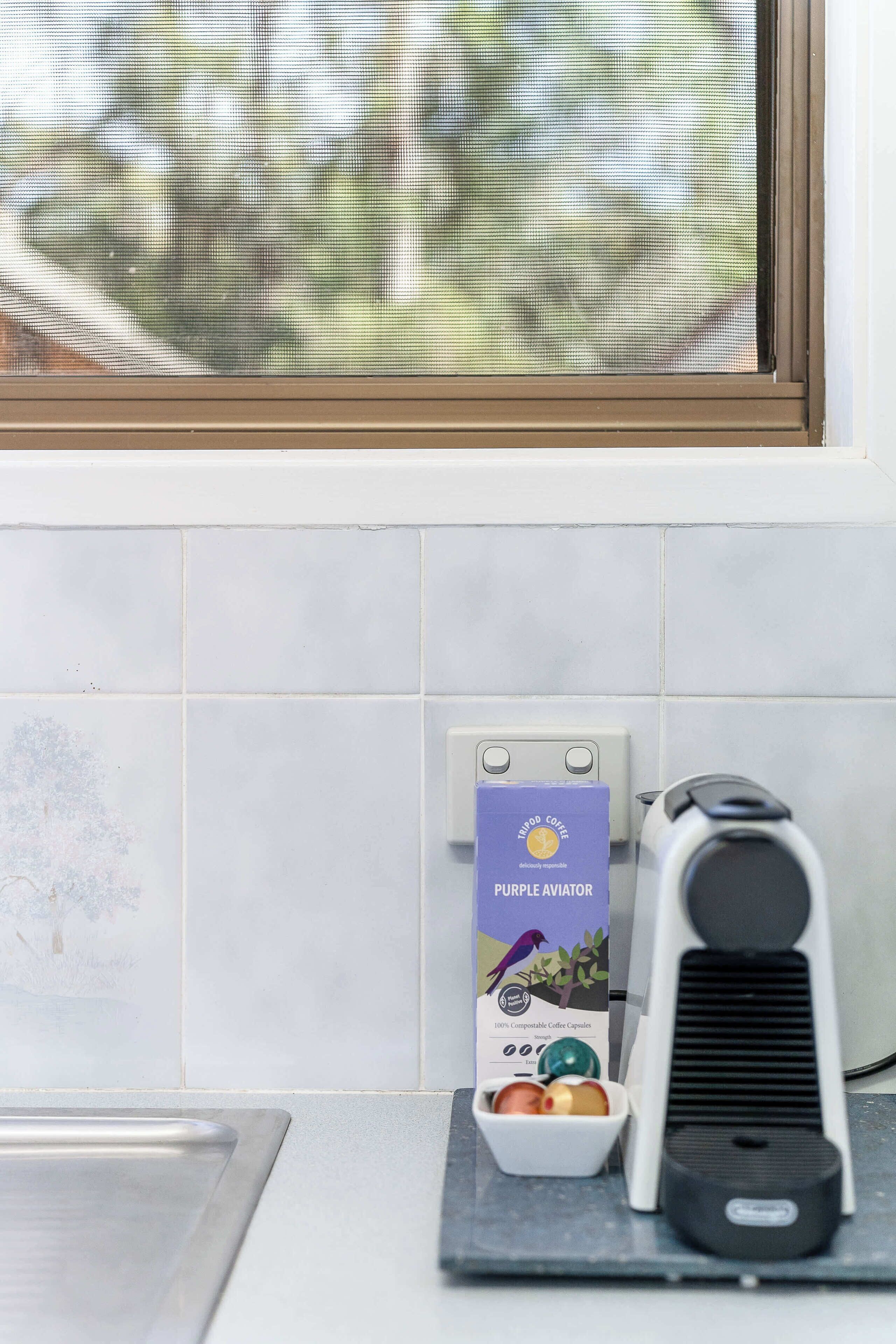 A coffee maker, a coffee capsule box, and a window with a view of trees.