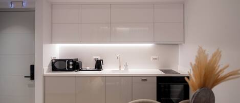 Een moderne keuken met witte kasten, een magnetron, een koffiezetapparaat en een spoelbak.