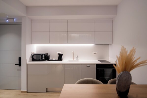 A modern kitchen with white cabinetry, a microwave, a coffee maker, and a sink.