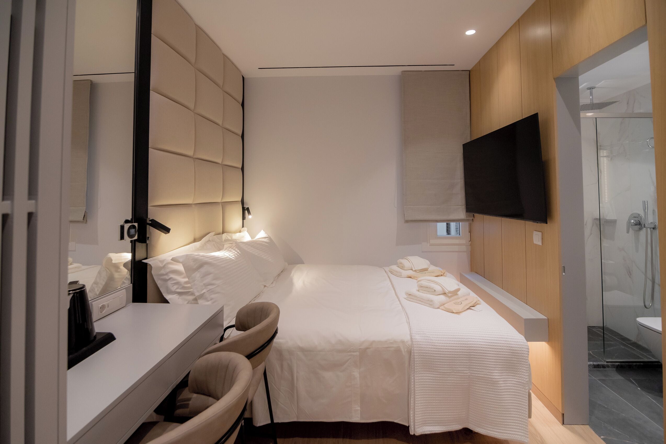 Moderni hotellihuone, jossa on suuri sänky, työpöytä tuolilla, taulutelevisio ja suihkutila.
