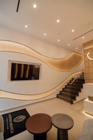 Una moderna hall d'albergo con una scala a forma di curva, una reception e un'area salotto con due tavoli rotondi.