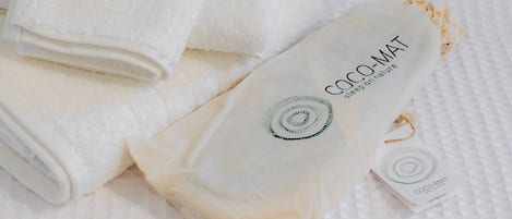 A bed with a white quilted mattress and a folded white towel. A white pillow with the text "COCO-MAT" and "sleep on nature" is placed on the bed.