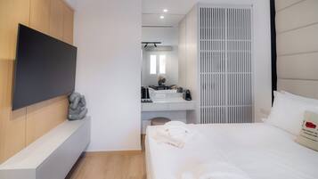 Una habitación de hotel moderna con una cama grande, un televisor de pantalla plana montado en la pared, un escritorio con computadora y un armario.