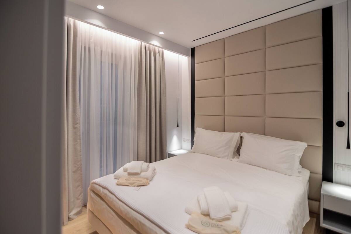 A modern hotel room with a large bed, a padded headboard, and a bedside table.