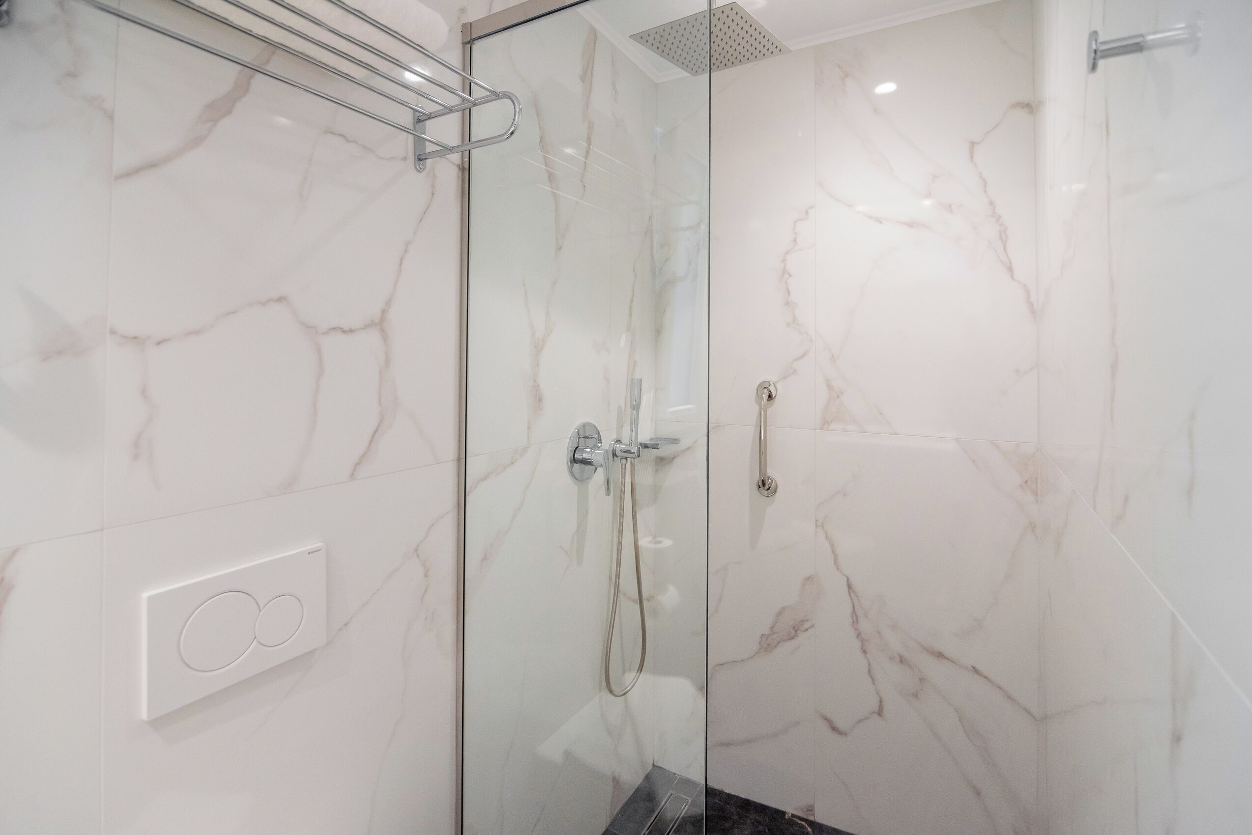 A modern bathroom with a glass shower enclosure, marble walls, and a visible control panel.