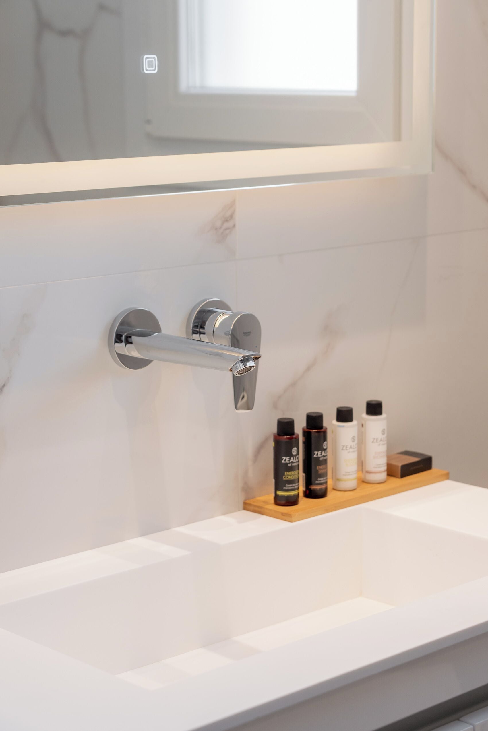 A bathroom with a white marble wall, a chrome towel rack, and a wooden shelf with skincare products.