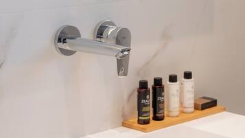 A bathroom with a white marble wall, a chrome towel rack, and a wooden shelf with skincare products.