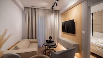 Een moderne hotelkamer met een bank, een klein rond tafeltje, een flatscreen televisie aan de muur en een bed met hoofdeinde.