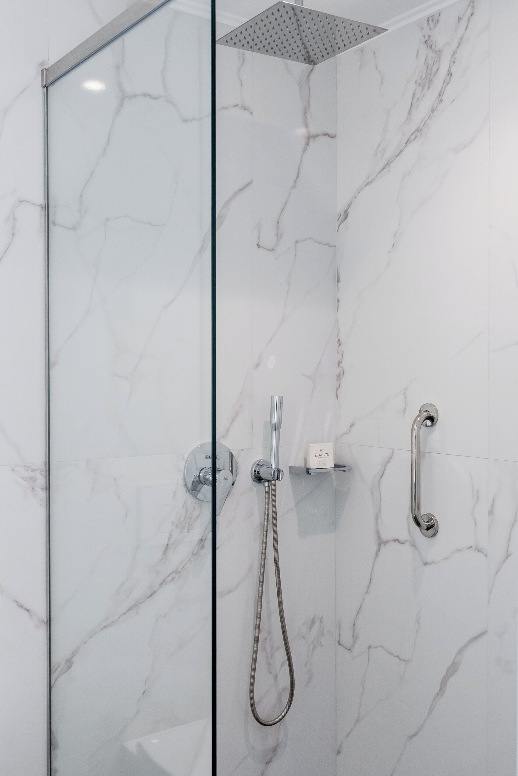 Une douche fermée par des parois en verre, dotée d’un pommeau de douche à main et d’un robinet à main.