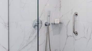 A glass-enclosed shower with a handheld showerhead and a handheld faucet.