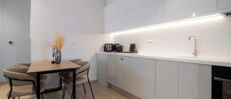 A modern kitchen with white cabinets, a wooden dining table, and a coffee machine.