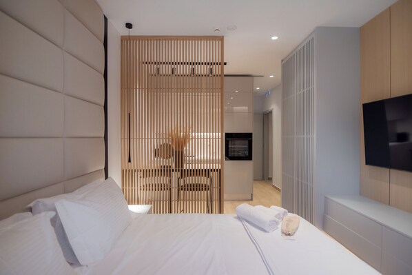 Una habitación de hotel moderna con una cama grande, un televisor montado en la pared y un panel de madera que separa la habitación del pasillo.