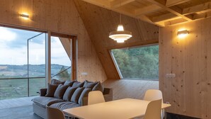 Un interior moderno con techo de madera, una mesa de comedor con sillas, un sofá y un amplio ventanal que ofrece vistas al exterior.