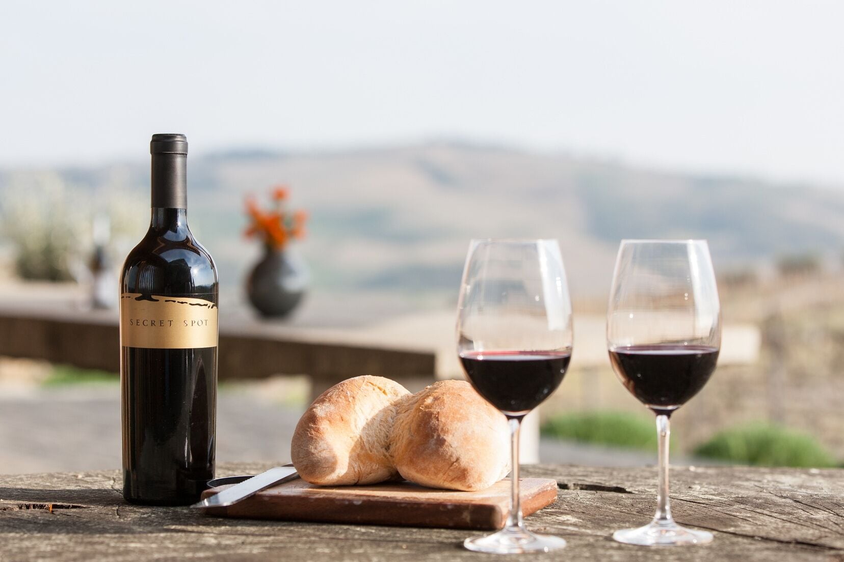 A bottle of wine, two glasses of red wine, and a loaf of bread on a wooden table with a rustic background.