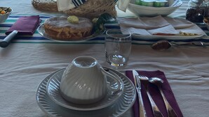 Mesa servida con un plato, una copa, una jarra y una cesta de pan, con vistas al campo.