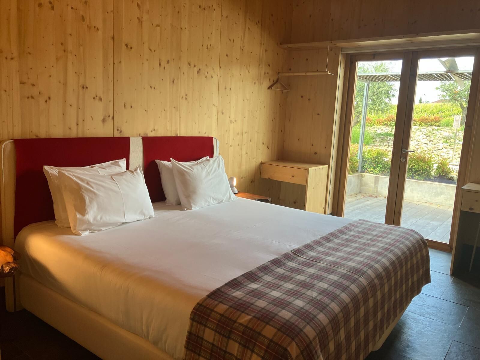 Una habitación con paneles de madera, una cama, una mesita de noche y un ventanal con vistas a la vegetación.