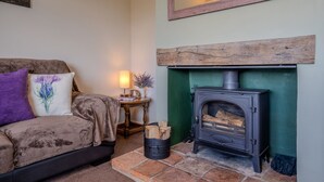 A cozy living room with a sofa, a table with a lamp, and a wood-burning stove.