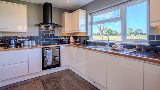 A modern kitchen with white cabinets, a black range hood, a built-in oven, and a large window offering a view of the outdoors.