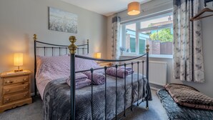 A neatly arranged bedroom with a metal bed frame, a bedside table with a lamp, a window with curtains, and a small bench.