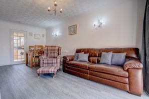 A living room with a brown leather sofa, plaid armchair, and a wooden table with chairs.