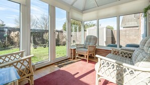 A conservatory with wicker furniture, large glass doors, and a view of a garden. - Swallowdale | East Ruston Cottages (Trunch)
