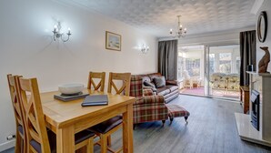 A dining area with a wooden table and chairs, a sofa, and a fireplace. - Swallowdale | East Ruston Cottages (Trunch)