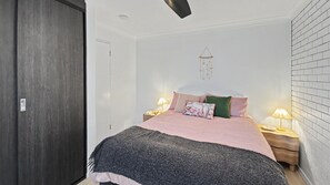 A bedroom with a bed, bedside lamps, a wall-mounted hanging, and a door.