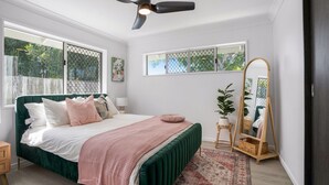 A bedroom with a green upholstered bed, a large mirror, and a view of greenery outside.