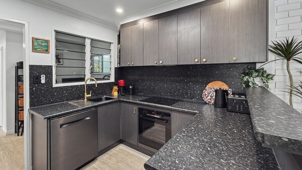 A modern kitchen with dark cabinetry, a granite countertop, and stainless steel appliances. - Vitamin Sea - Rainbow Beach (Rainbow Beach)