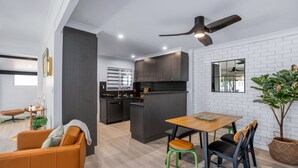 A modern kitchen with dark cabinets, a central island, and a dining area with a wooden table and chairs.