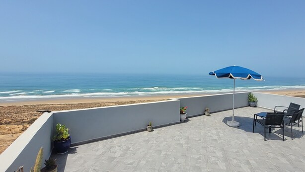 Una terrazza sul tetto con vista sulla spiaggia, un ombrellone blu e piante in vaso.