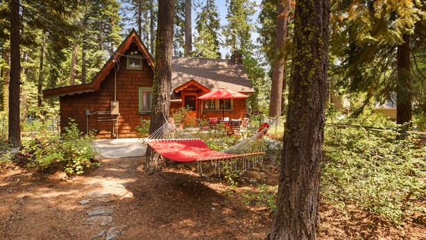 A cabin with a red roof and a hammock in front.