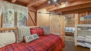A cozy cabin interior with a bed, a window with blinds, and a wooden ceiling.