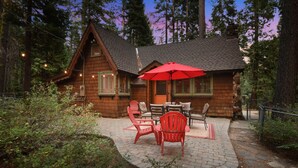 A wooden cabin with a patio area featuring outdoor seating and a red umbrella.