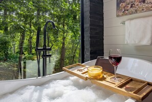 A bathtub filled with bubbles, a glass of red wine, and a tray with a candle and a glass. - Luxury Mountaintop Cabin • Pool w/ Rock Waterfall • Epic Views (Broken Bow)