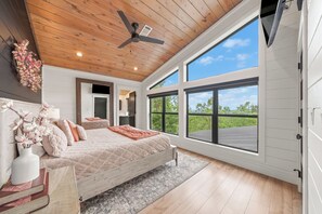 A bedroom with a bed, a ceiling fan, large windows, and a view of the outdoors. - Luxury Mountaintop Cabin • Pool w/ Rock Waterfall • Epic Views (Broken Bow)
