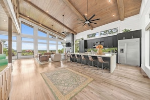 A spacious kitchen with a large island, dark cabinets, and a stainless steel refrigerator.