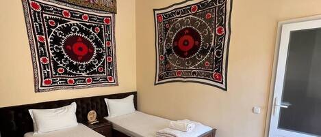 A hotel room with two single beds, a large window, and two wall tapestries.