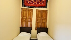 Une pièce étroite avec deux lits en bois, une moquette sombre et un plafond orné de motifs floraux.
